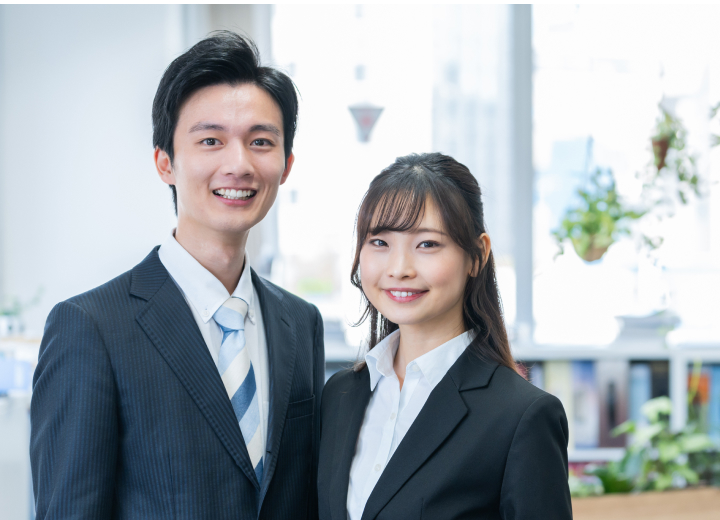 スーツ姿で正面を向き、笑顔を向ける男性社員と女性社員。私たちのチームに参加しませんか？